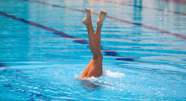 Synchronized swimmers legs point up out of the water in action