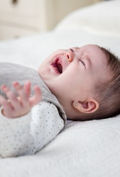 Cute baby girl crying over white bedcover