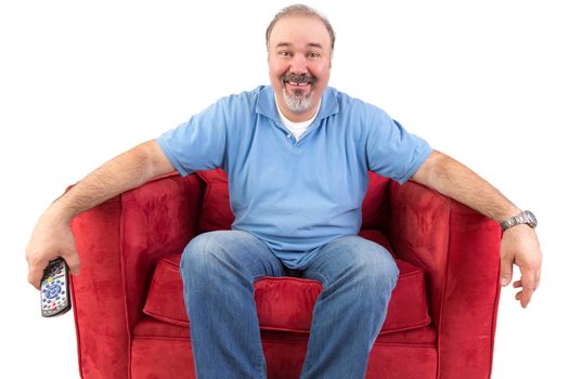 Funny cheerful middle-aged Caucasian man wearing casual clothes while sitting on a red comfortable armchair holding the remote control, on white background