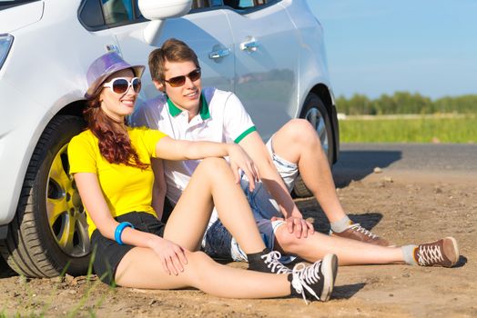 young couple sitting on the ground next to the wheel of a car, a summer road trip