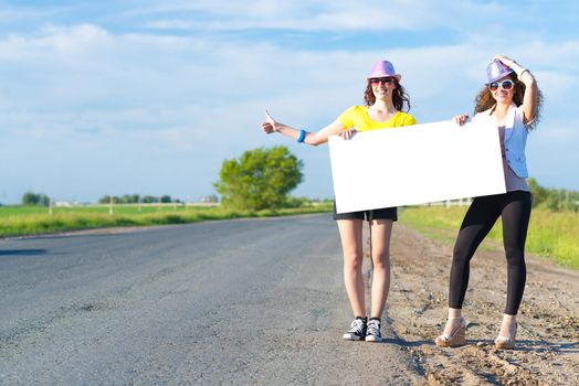 Two young women stand with a blank banner on the side of the road, place for text