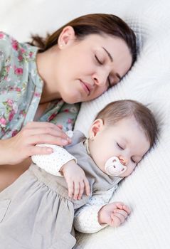 Young mother and her cute baby girl sleeping together in the bed