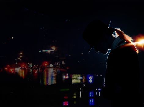 Silhouette of the woman with hat standing in the night city with illumination