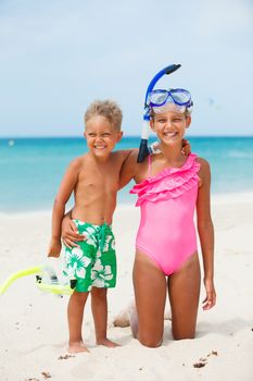 Two happy children on beach with colorful face masks and snorkels, sea in background.