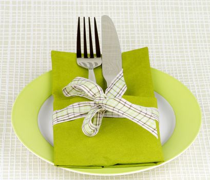Elegant Table Setting with Fork and Table Knife into Green Napkin Decorated with Green Checkered Bow on Green Plate
