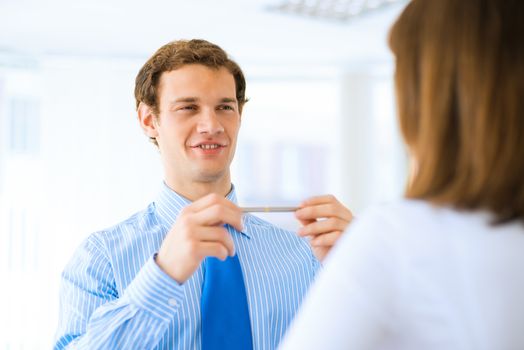 young businessman holds up a pen, talking with a colleague in front of