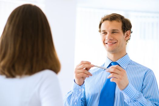 young businessman holds up a pen, talking with a colleague in front of