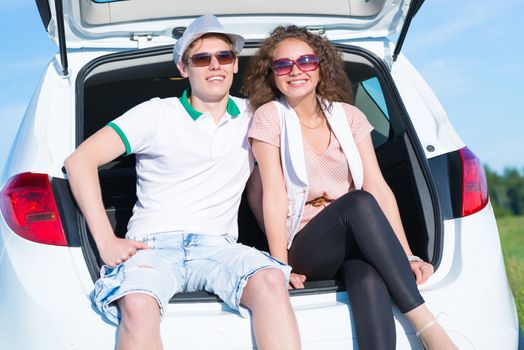 young couple sitting in the open trunk of a new car, a summer road trip