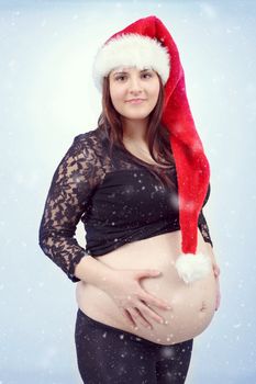 beautiful smiling pregnant young santa woman tenderly holding her tummy with snowing in background