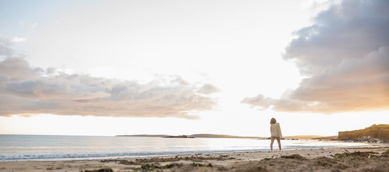 Full length of a young woman in sweater walking on the beach