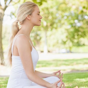 Side view of ponytailed calm woman meditating sitting in a park with closed eyes