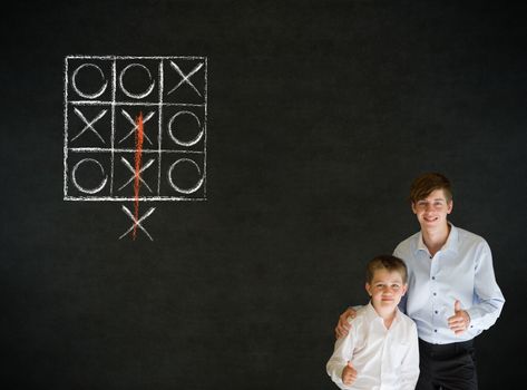 Thumbs up boy dressed up as business man with teacher man and thinking out of the box tic tac toe concept on blackboard background