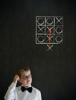 Scratching head thinking boy dressed up as business man with thinking out of the box tic tac toe concept on blackboard background