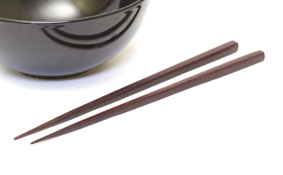 Dark wooden chopsticks and ceramic bowl on white background