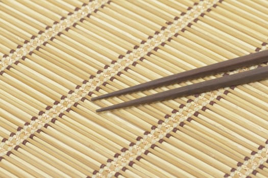 Dark wooden chopsticks on bamboo mat