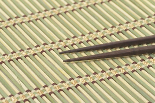 Dark wooden chopsticks on bamboo mat