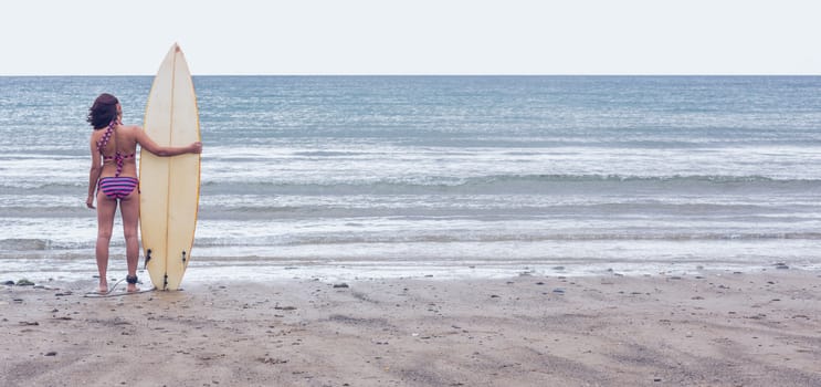 Rear view of a calm woman in bikini with surfboard on beach