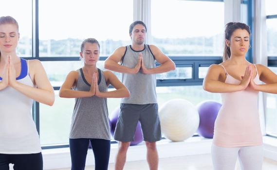 Fitness class and instructor standing in Namaste position at  exercise studio