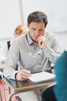 Focused handsome mature student sitting in classroom with classmates while learning