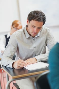 Concentrated male mature student sitting in classroom with classmates while learning