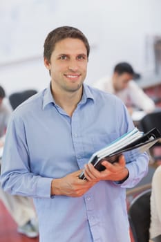 Cute male teacher holding some files while posing in his classroom and smiling at camera