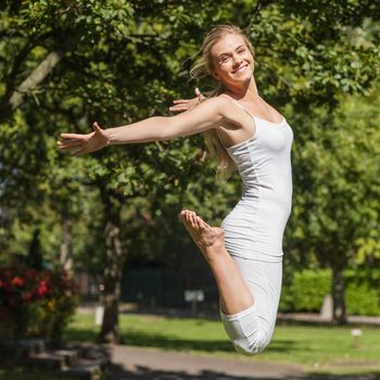 Side view of young fit woman jumping spreading her arms in a park