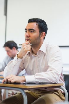 Thoughtful mature student taking notes with others in lecture in college