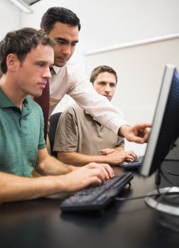 Teacher showing something on screen to mature students in the computer room