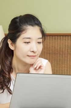 happy young asian woman working with laptop in bedroom
