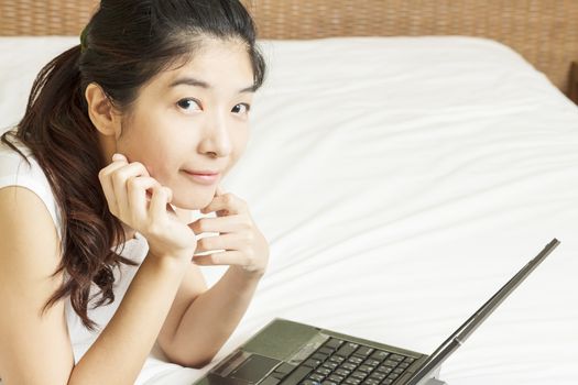 happy young asian woman working with laptop in bedroom