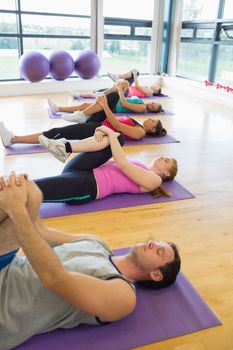 Sporty people doing the supine wind release posture at yoga class in fitness studio