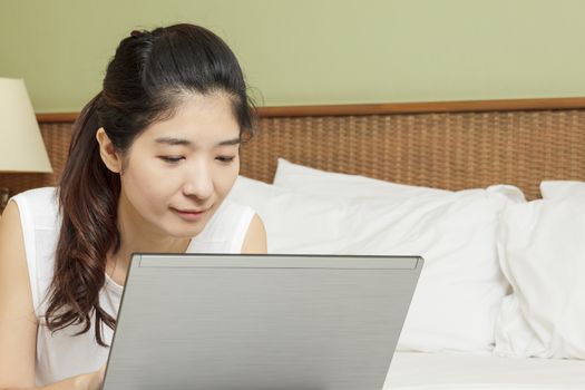 happy young asian woman working with laptop in bedroom