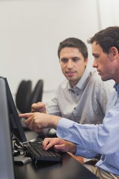 Two mature men talking while sitting in front of computer in computer class