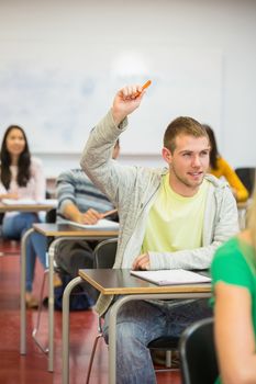 Young male student raising hand by others in the college classroom