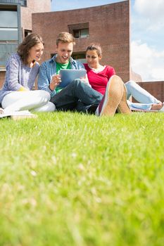 Group of young students using tablet PC in the lawn against college building