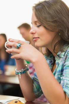 Close up of a female having coffee and muffin with students around table in background at  the coffee shop