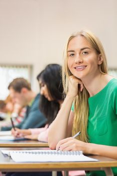 Portrait of a young female student with others writing notes in the classroom