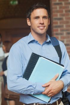 Attractive mature student posing in corridor holding some files looking at camera