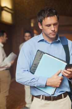 Serious handsome mature student using his smartphone standing on he corridor