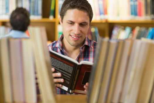 Close up of a concentrated mature student reading book by shelf in the library