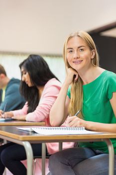 Portrait of a young female student with others writing notes in the classroom