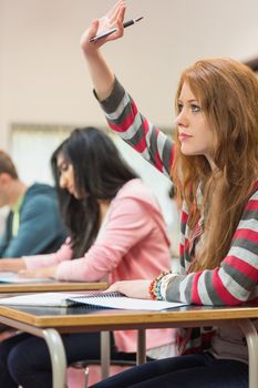 Side view of a young female student raising hand by others in the classroom