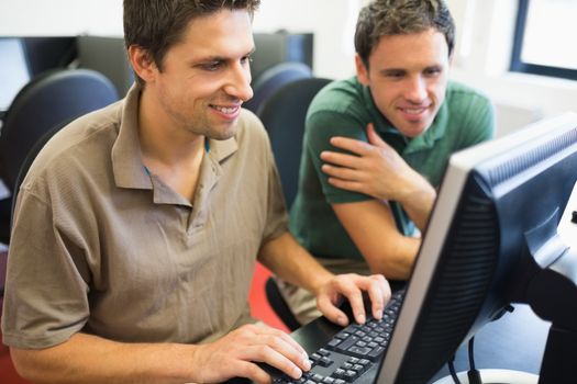 Smiling teacher and mature student using computer in the computer room