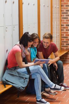 Smiling students sitting on bench using tablet in school