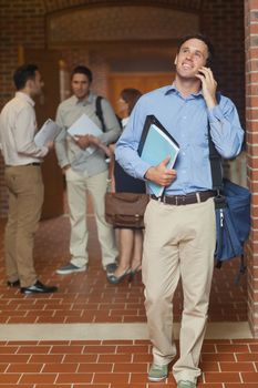 Cheerful handsome mature student phoning with his smartphone walking through the corridor