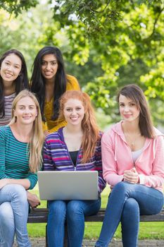 Group portrait of young college girls with laptop in the park