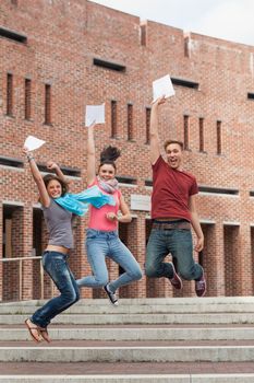 Happy students jumping in the air holding exam in school