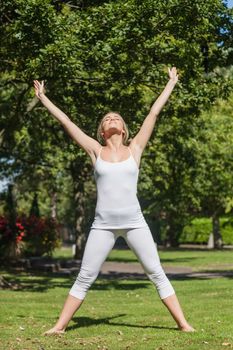 Blonde woman doing yoga in a park spreading her arms and legs