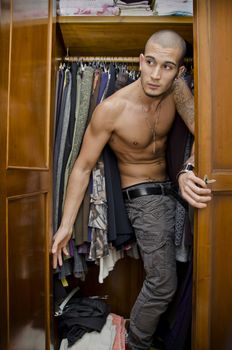 Handsome shirtless young male lover hiding from his woman's husband inside closet