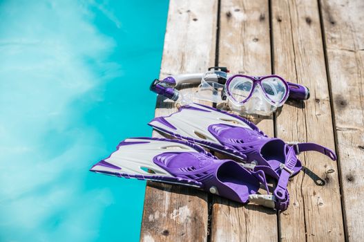Diver eyeglasses, diving goggles, scuba snorkel and fins or flippers on the jetty (wood deck) near the water